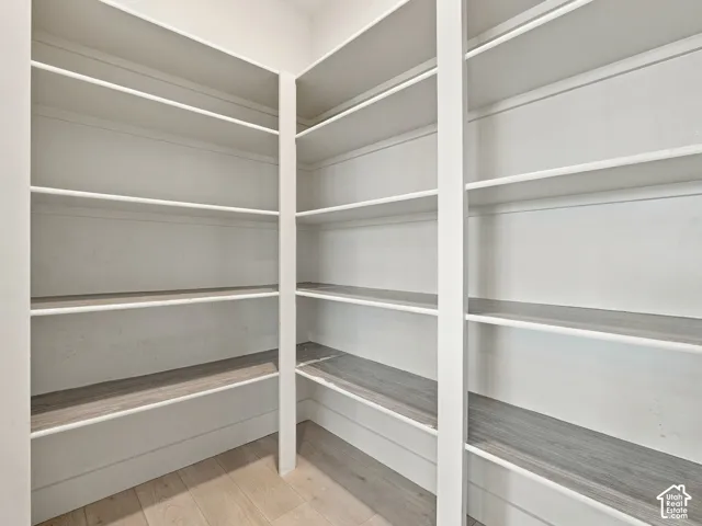 Walk-in pantry featuring white custom built-in shelving, wood-finish flooring, and multi-tier storage configurations