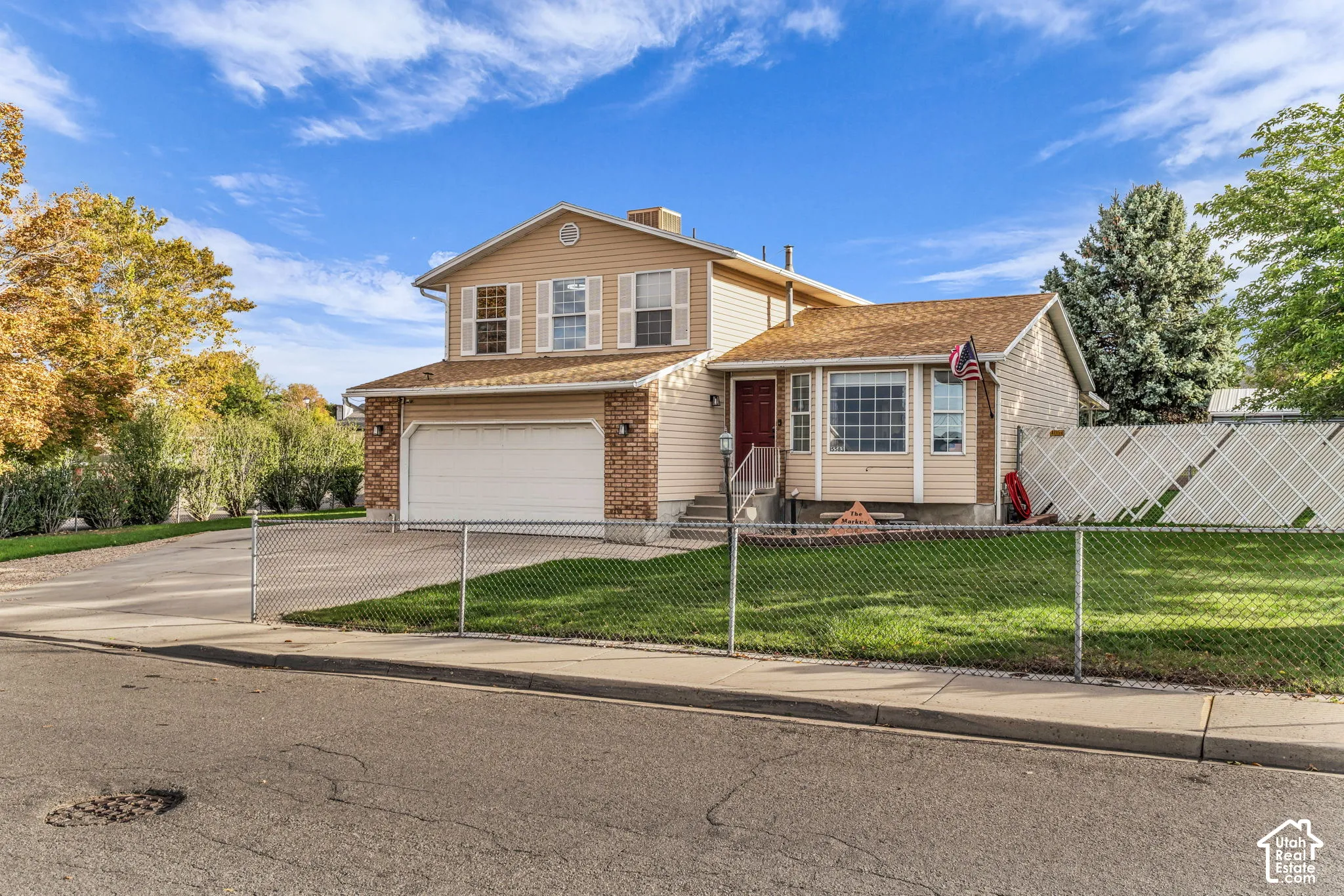 Two-story exterior featuring tan horizontal siding, brick veneer accents, an attached two-car garage, and a fenced front yard with a concrete driveway