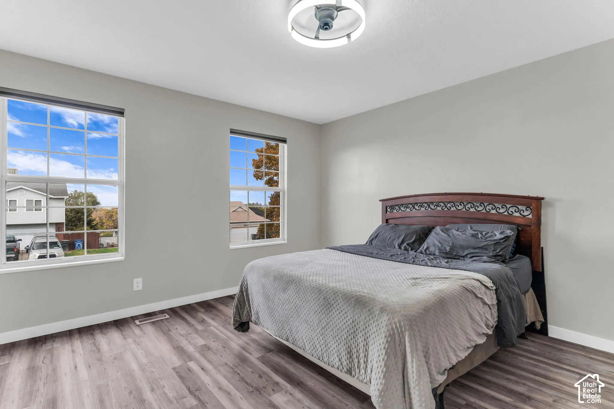 Wood-finish flooring, neutral wall tones, two large dual-pane windows with muntins, and a contemporary circular flush-mount ceiling fixture