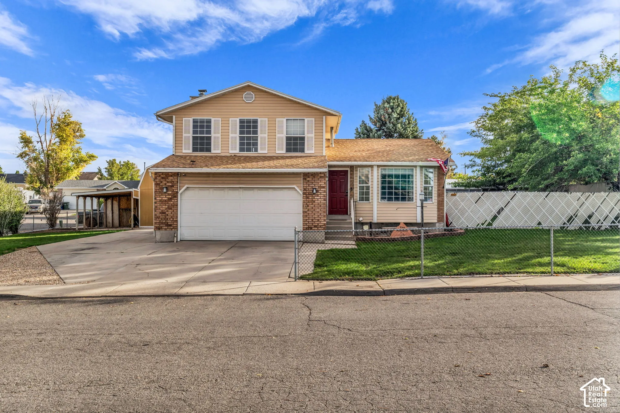 Two-story residence with a brick and lap-siding exterior, attached multi-car garage, concrete driveway, and white lattice fencing