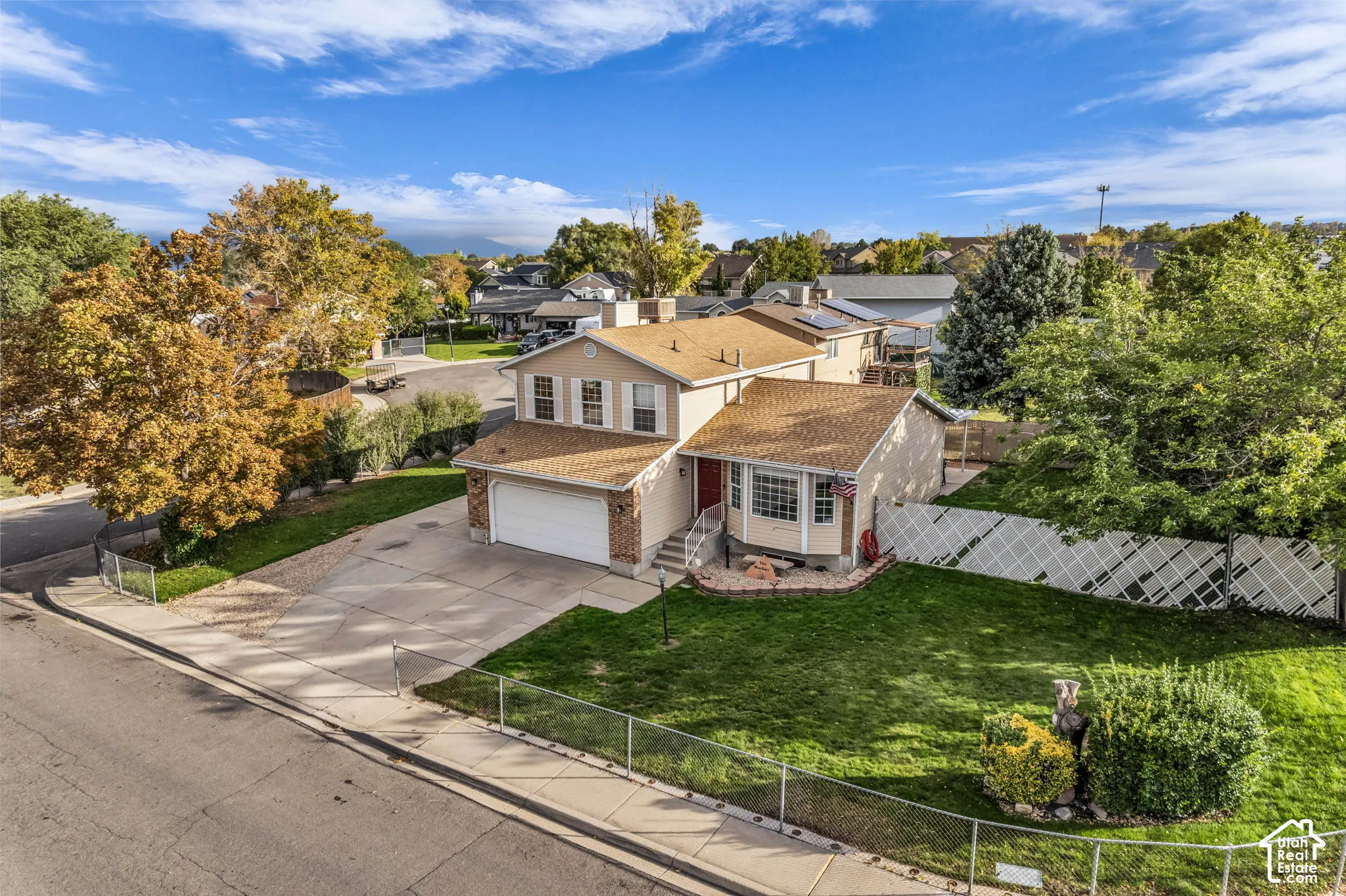 Split-level residence featuring a two-car garage, shingled roof, neutral-tone siding, decorative shutters, and a fenced yard with mature landscaping