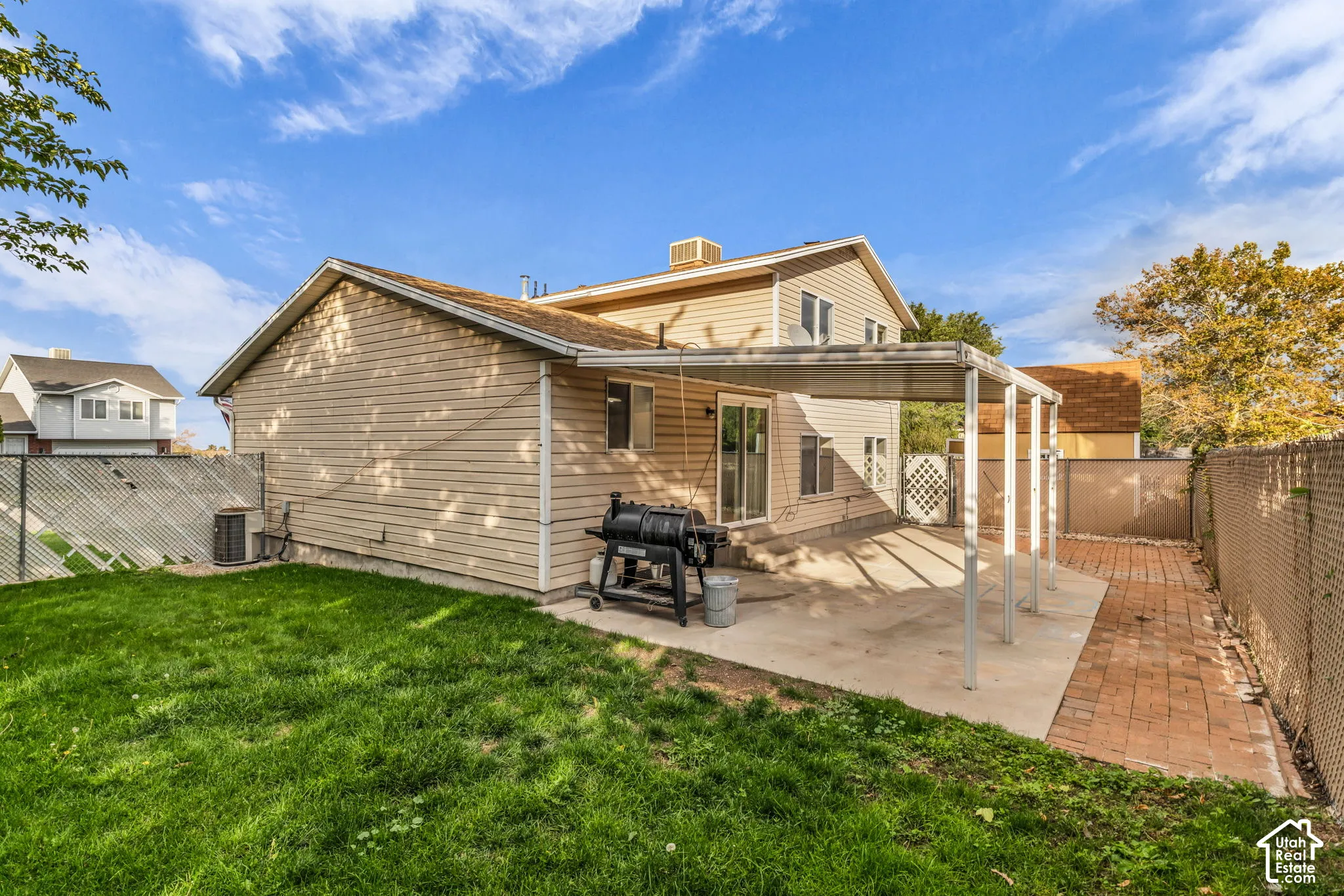 Exterior featuring beige horizontal siding, a concrete patio, a covered patio structure, a brick-paver pathway, and a fenced backyard with lawn