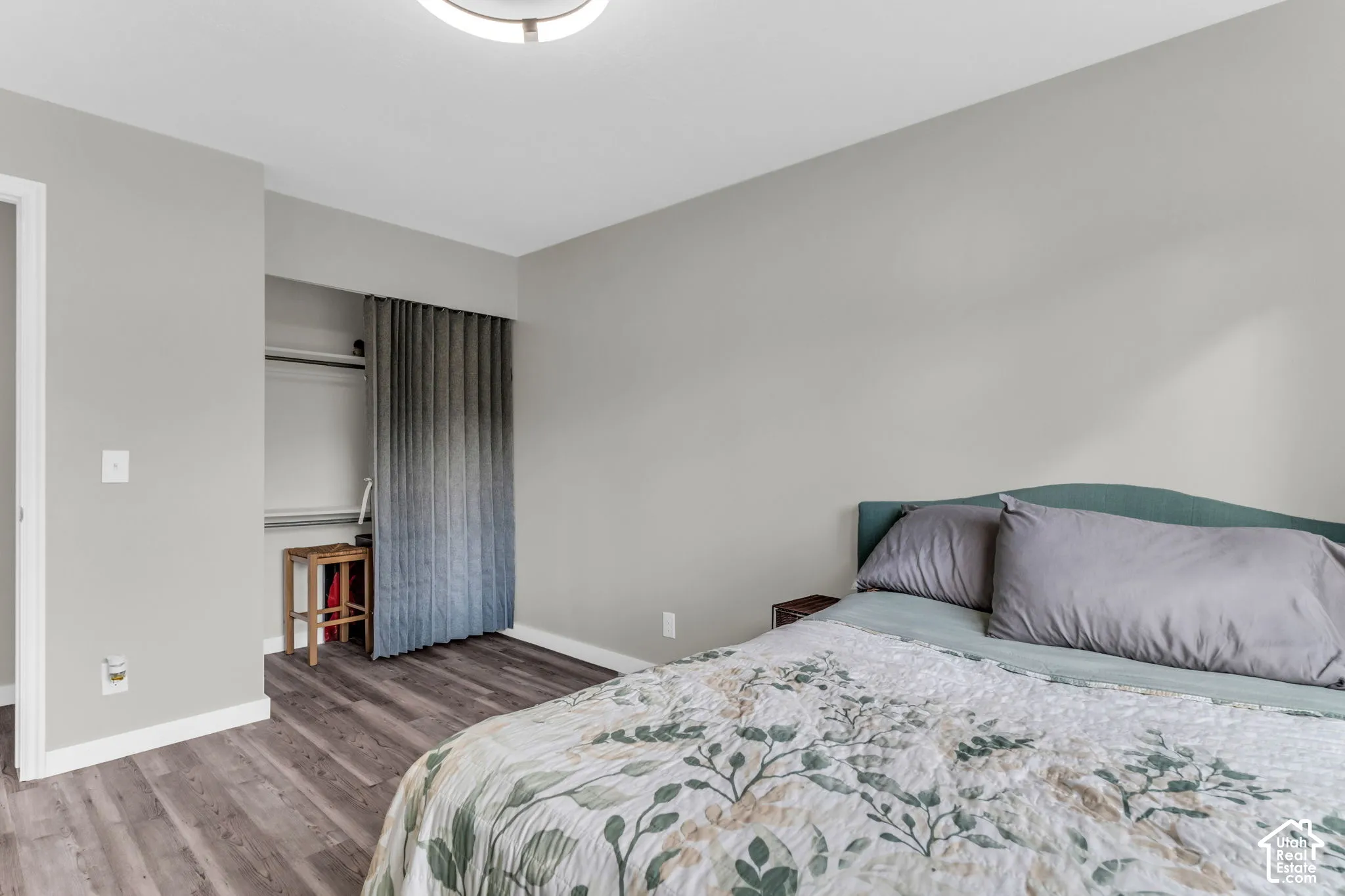 Neutral-toned walls, wood-finish flooring, and a recessed closet area featuring a sliding fabric door panel