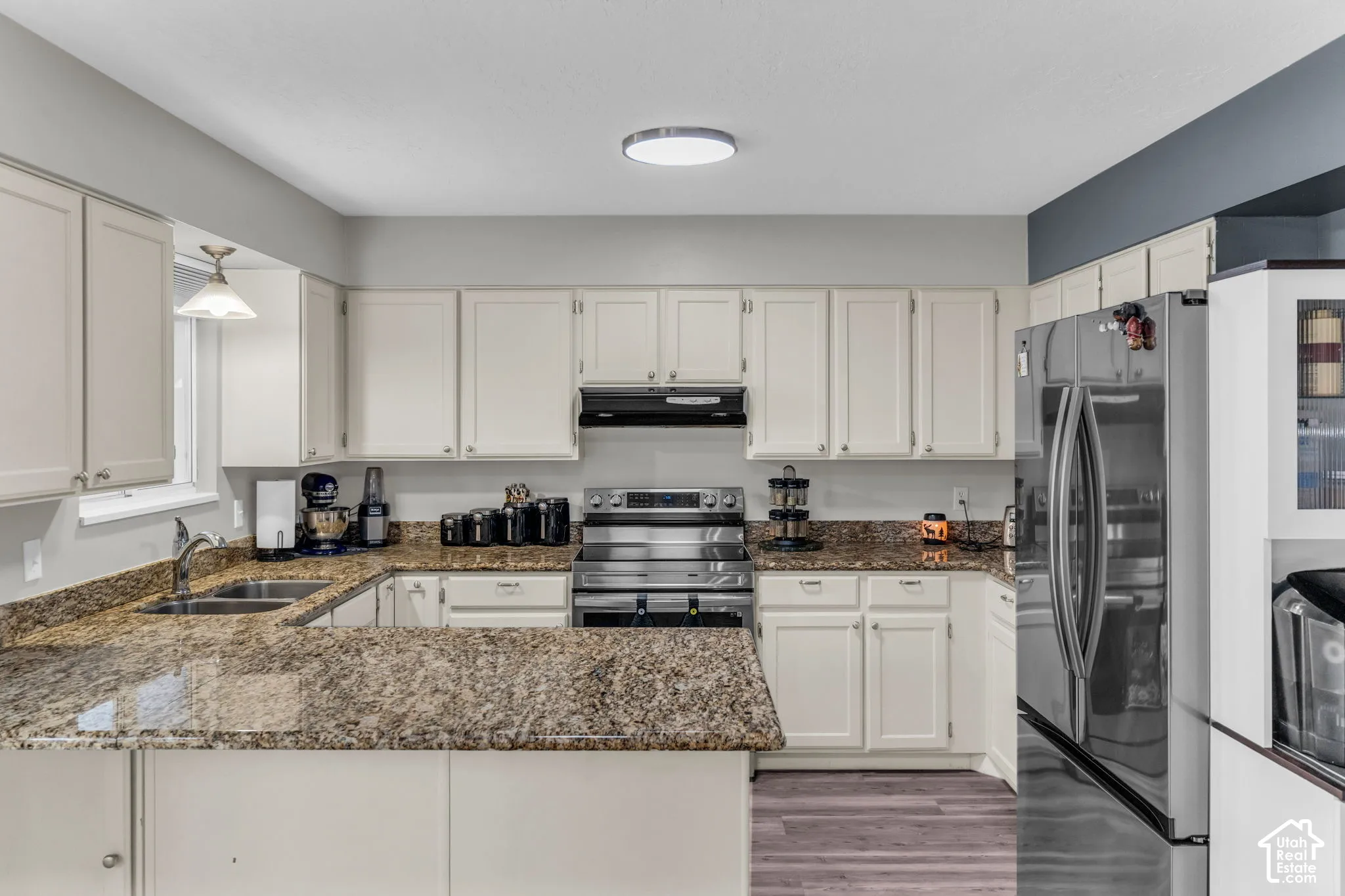 Kitchen featuring light-toned cabinetry, stone-surface countertops, stainless steel appliances, a dual-basin sink, and wood-finish flooring
