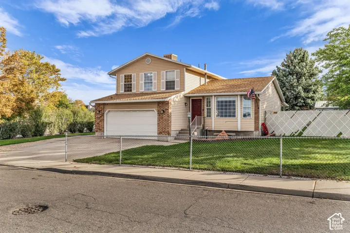 Two-story exterior featuring tan horizontal siding, brick veneer accents, an attached two-car garage, and a fenced front yard with a concrete driveway