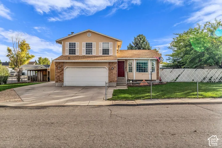 Two-story residence with a brick and lap-siding exterior, attached multi-car garage, concrete driveway, and white lattice fencing