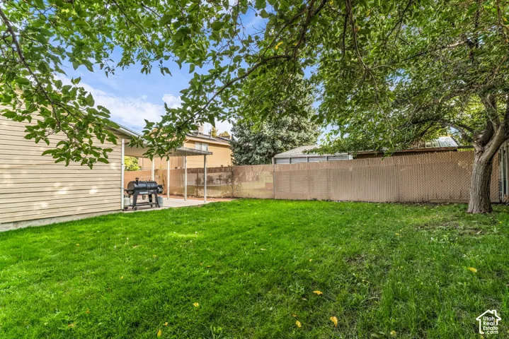 Backyard featuring a grass lawn, mature trees, concrete patio, and a privacy fence