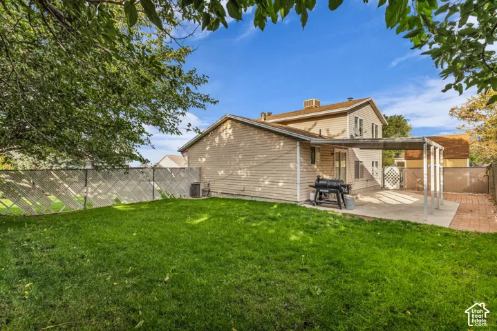 Backyard featuring a concrete patio with a metal-frame cover, a brick-paved walkway, and perimeter lattice fencing