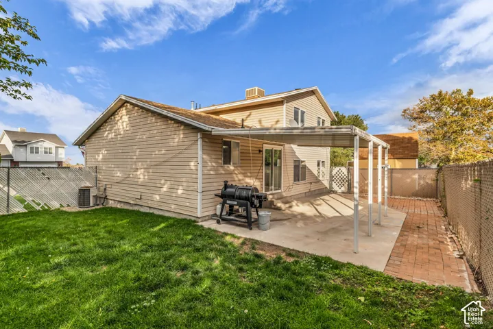 Exterior featuring beige horizontal siding, a concrete patio, a covered patio structure, a brick-paver pathway, and a fenced backyard with lawn