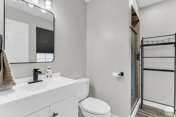 Bathroom featuring a white vanity with a rectangular sink, matte black faucet, rectangular mirror with a rounded black frame, and wood-finish flooring