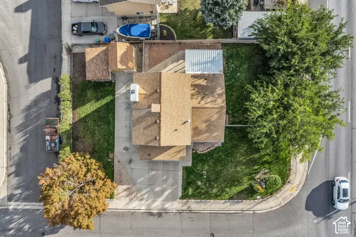 Corner lot featuring a concrete driveway, detached storage structure, metal-roofed patio cover, and mature landscaping