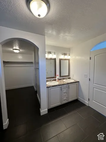 Dual-sink vanity with stone-surfaced countertop, two framed mirrors, multi-bulb vanity lighting, and large-format tile flooring
