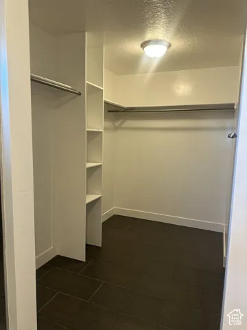 Walk-in closet featuring large-format tile flooring, built-in shelving, dual metal hanging rods, and a flush-mount overhead light fixture