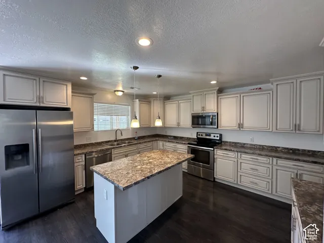 Kitchen featuring light-toned cabinetry, patterned stone-finish countertops, stainless steel appliances, a central island, and wood-finish flooring