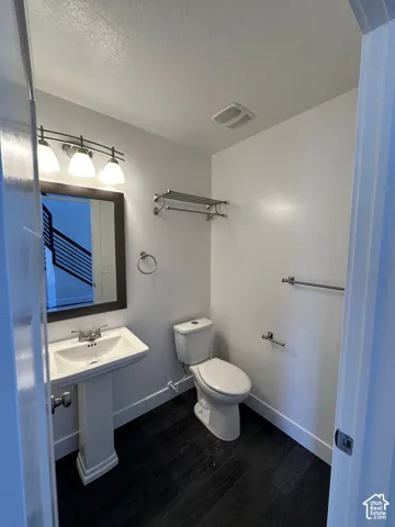 Pedestal sink with chrome faucet, framed vanity mirror, three-light fixture, wall-mounted shelving, and wood-finish flooring