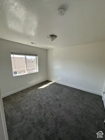 Neutral-toned interior space featuring plush carpeting, crisp white walls, and a window with fitted blinds