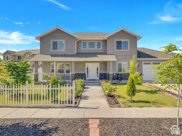 Two-story exterior featuring a stone-veneer foundation, covered front porch, white picket fencing, and attached multi-car garage