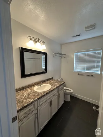 Bathroom vanity featuring a stone-patterned countertop, an integrated oval basin, light-finished cabinetry, a tri-light fixture, and dark-toned floor tiling