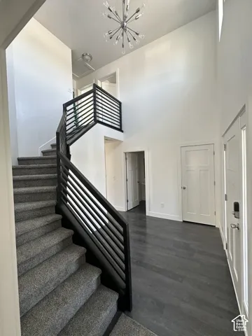 Entryway featuring high ceilings, dark wood-finish flooring, a staircase with a horizontal slat railing, and a multi-bulb sputnik chandelier