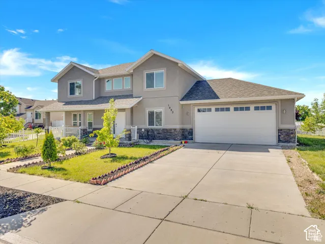 Two-story residence featuring a multi-gabled roofline, stone veneer siding, concrete driveway, attached three-car garage, and front porch with white railing
