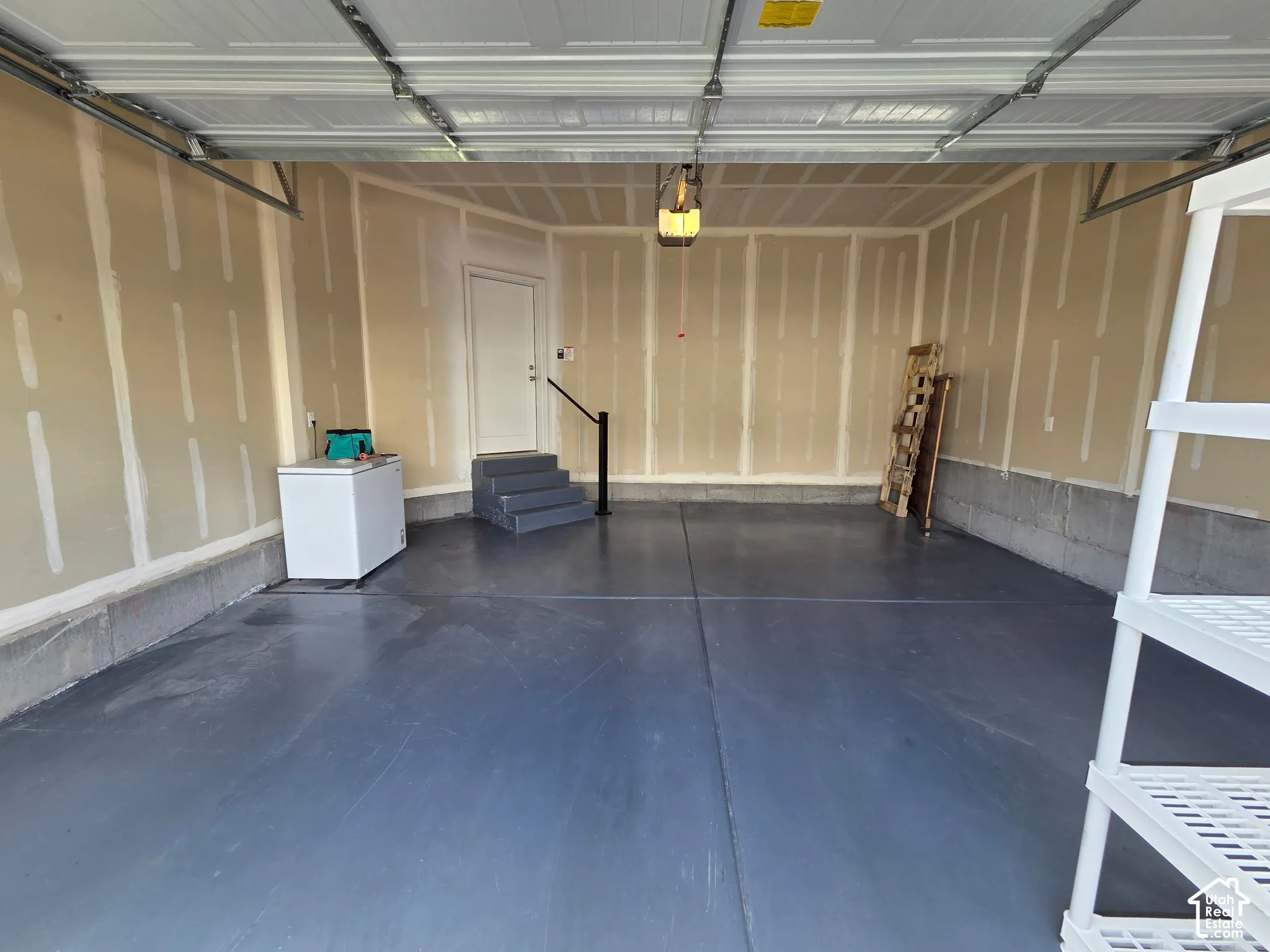 Finished two-car garage featuring sealed concrete flooring, drywall construction, and a dedicated pedestrian entrance with stairs and a handrail