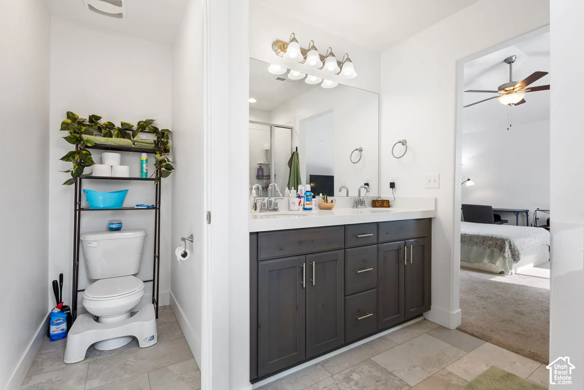 Bathroom vanity featuring deep-toned cabinetry, dual undermount sinks, solid-surface countertops, large-format tile flooring, and polished chrome light fixtures