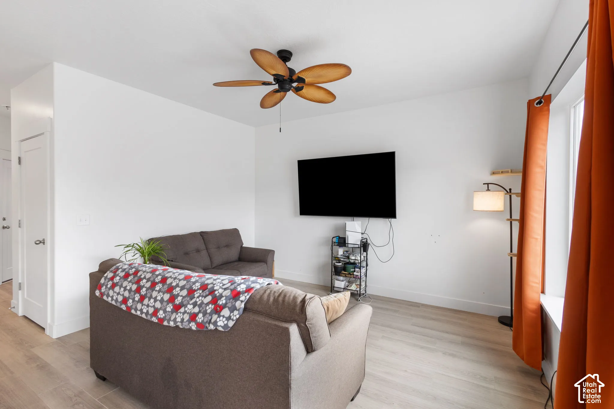 Neutral interior space featuring wood-finish flooring, a ceiling-mounted fan with five curved blades, and a solid-core interior door