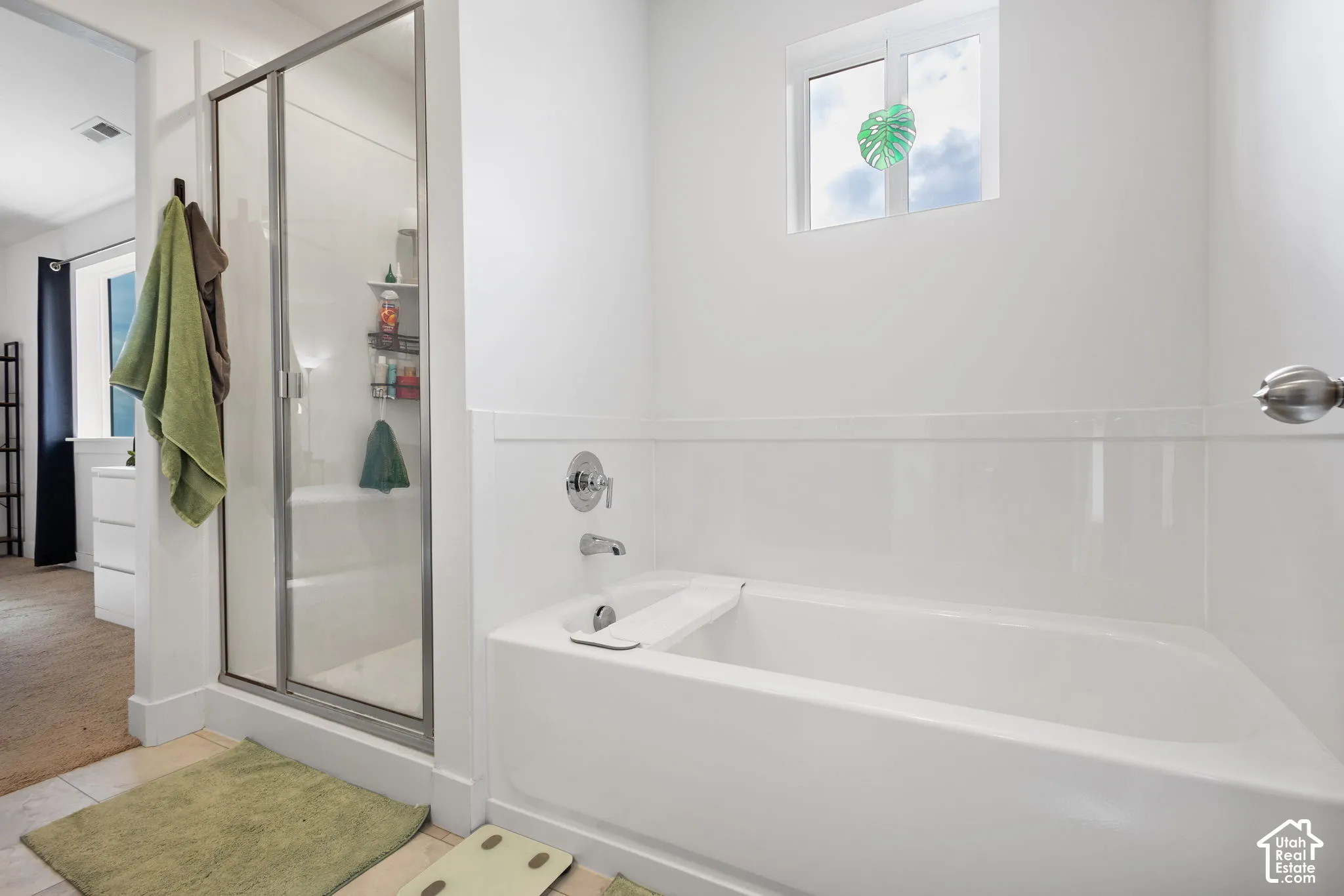 Full bathroom featuring a white porcelain tub, separate glass-enclosed shower, polished metal fixtures, and a dual-pane window