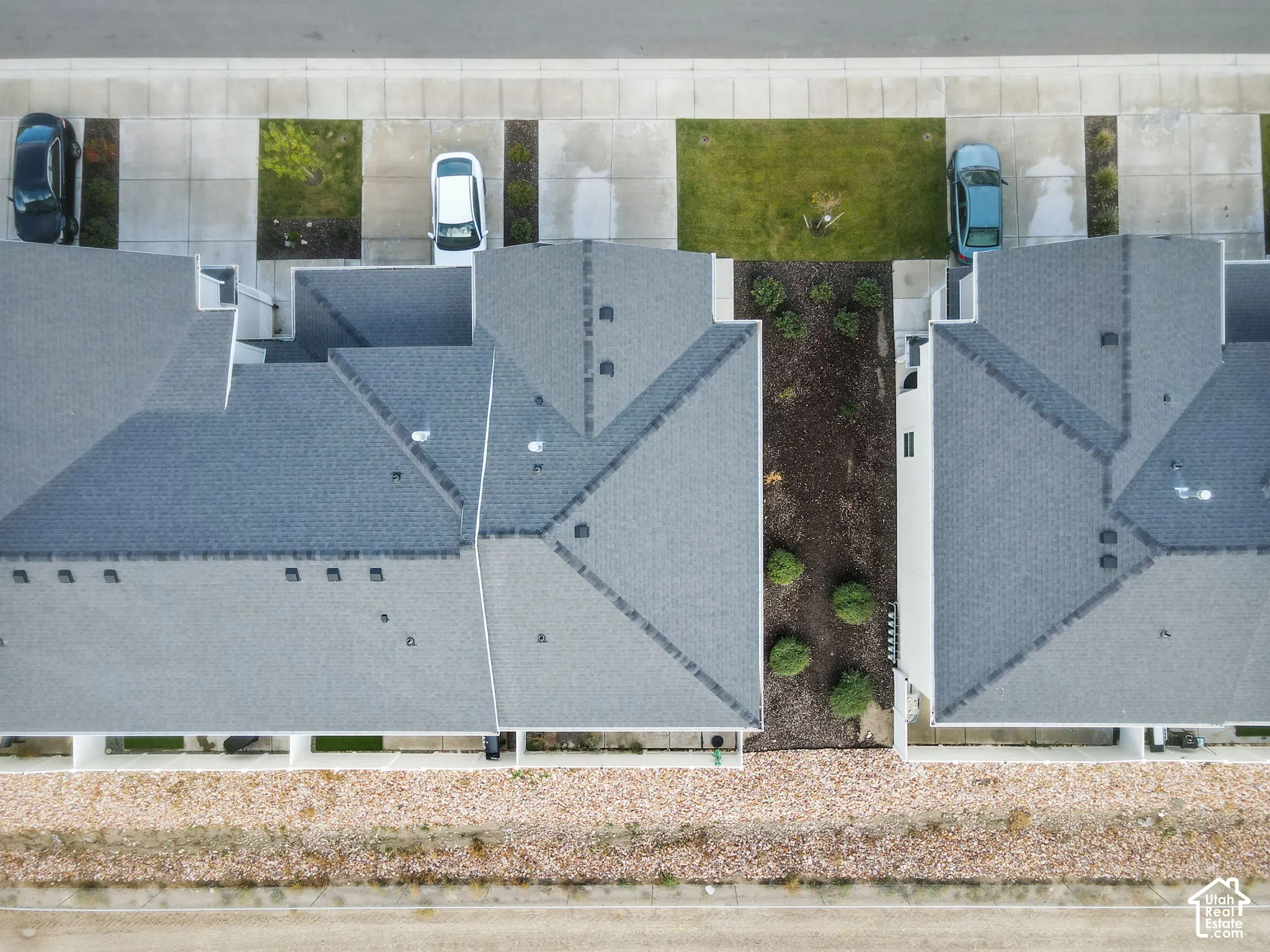 Aerial perspective of the property featuring a multi-pitched shingle roof, concrete driveway, and low-maintenance landscaping with rock ground cover