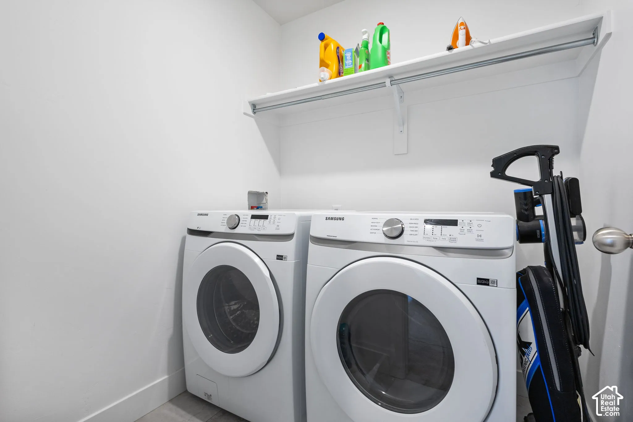 Laundry area featuring white front-load appliances and a mounted upper storage shelf with integrated hanging rod