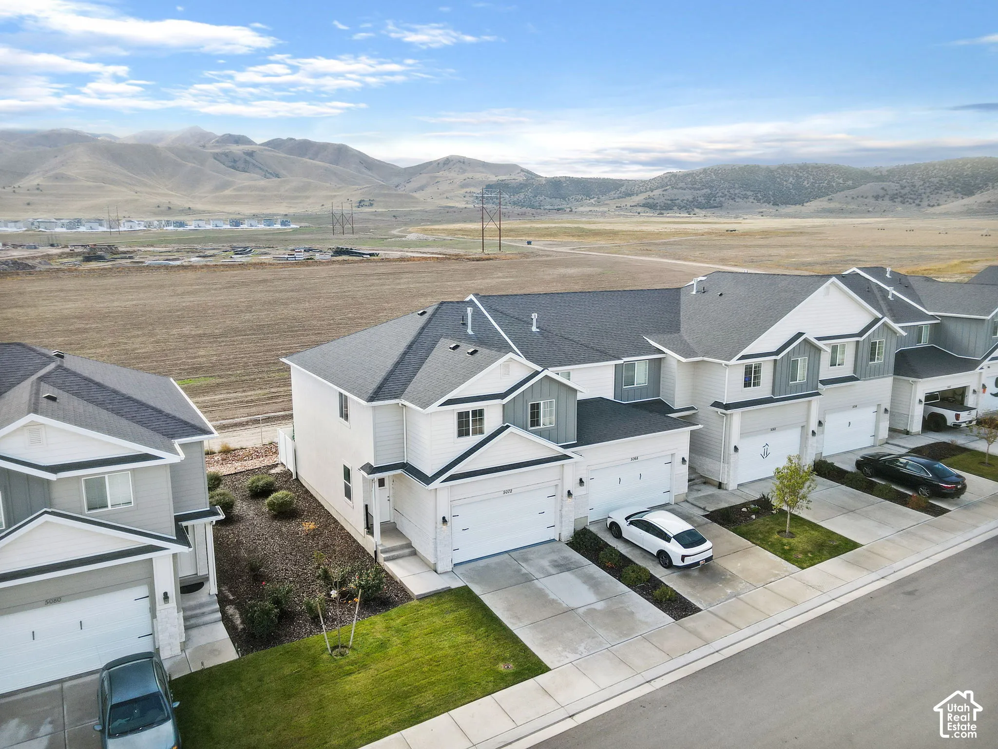 Multi-level exterior featuring light-toned horizontal siding, dark asphalt shingle roofing, attached two-car garages, and concrete driveways, set against a backdrop of mountain terrain