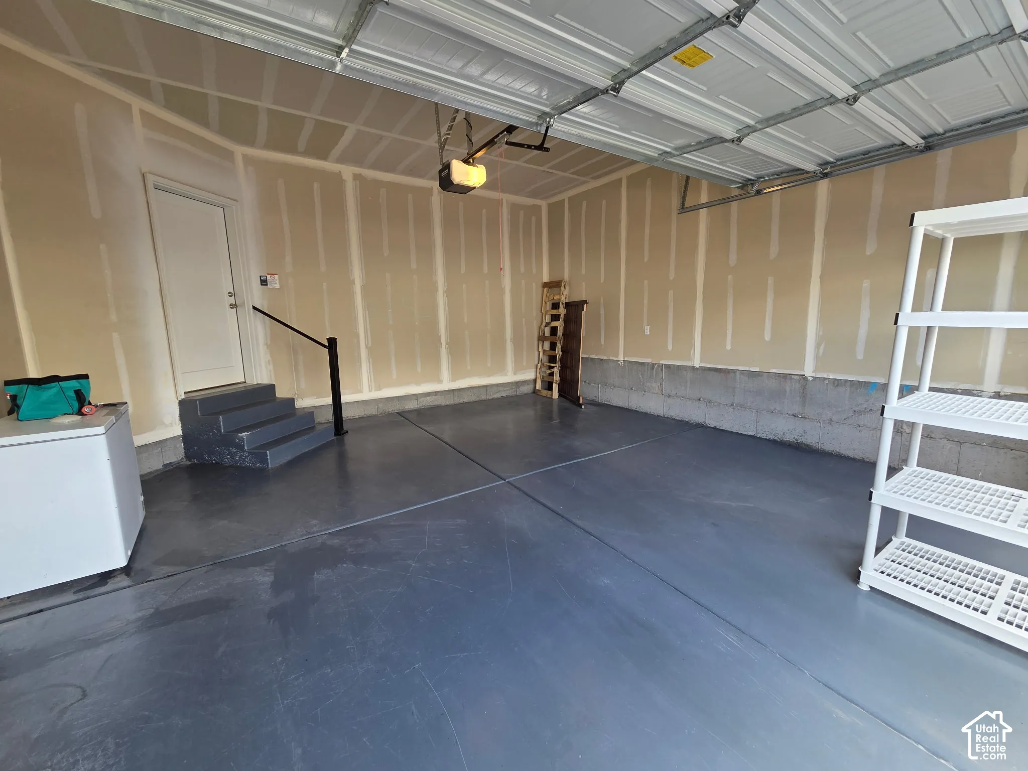 Two-car garage featuring a smooth epoxy-coated concrete floor, an overhead door opener, and a set of interior stairs with a black metal handrail