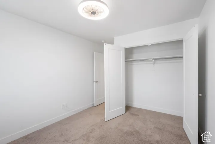 Interior room featuring neutral carpeting, a dual-panel closet door, solid-core interior doors, and a flush-mount ceiling fan with integrated lighting