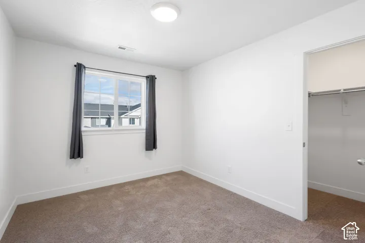 Neutral-toned carpeting, crisp white wall finish, window with divided lites, and a walk-in closet with integrated shelving