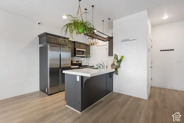 Kitchen featuring dark wood cabinetry, stainless steel appliances, a peninsula with a white countertop, and wood-finish flooring