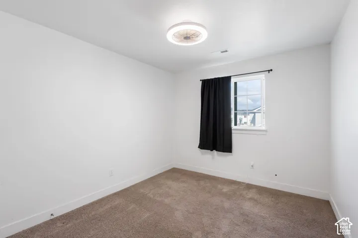 Neutral-toned interior room featuring wall-to-wall carpeting and a ceiling-mounted light fixture with an integrated fan