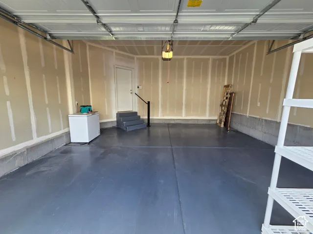Finished two-car garage featuring sealed concrete flooring, drywall construction, and a dedicated pedestrian entrance with stairs and a handrail