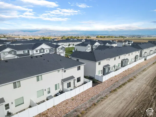 Aerial perspective featuring multi-story residential structures with dark asphalt shingle roofing, light-toned siding, white vinyl perimeter fencing, and a mountain range backdrop