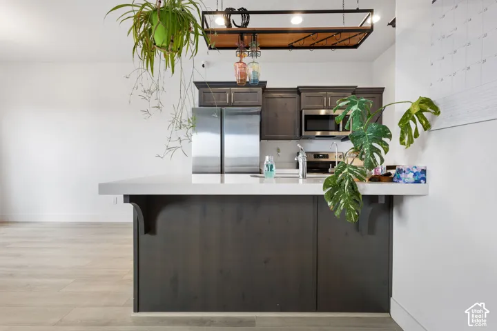 Kitchen featuring a peninsula with a quartz countertop, dark-toned cabinetry, stainless steel appliances, and a suspended metal rack