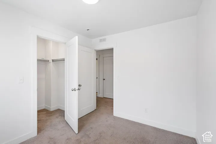 Interior room featuring neutral wall-to-wall carpeting, crisp white walls, minimalist shaker-style interior doors with brushed nickel hardware, and an open closet with built-in shelving