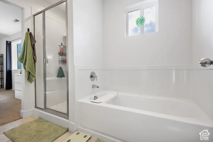 Full bathroom featuring a white porcelain tub, separate glass-enclosed shower, polished metal fixtures, and a dual-pane window