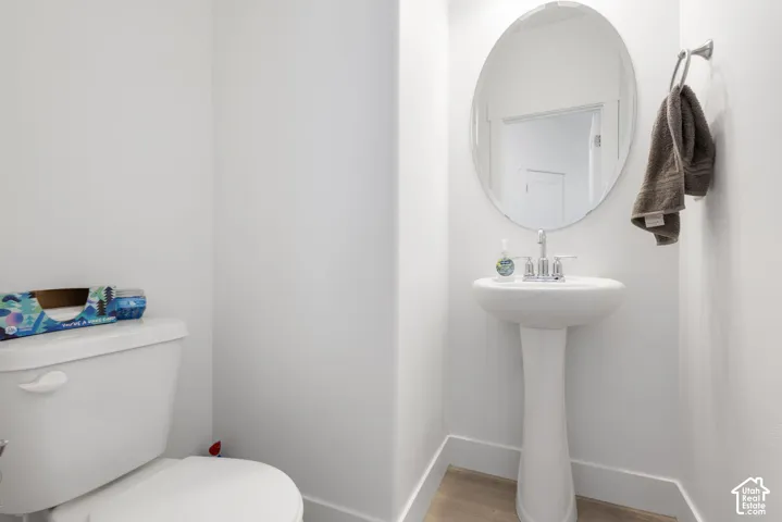 Pedestal sink featuring a polished chrome faucet, oval wall-mounted mirror, and wood-finish flooring