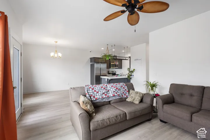 Wood-finish flooring, ceiling fan with palm-style blades, kitchen featuring dark cabinetry and stainless steel appliances, and a polished metal chandelier