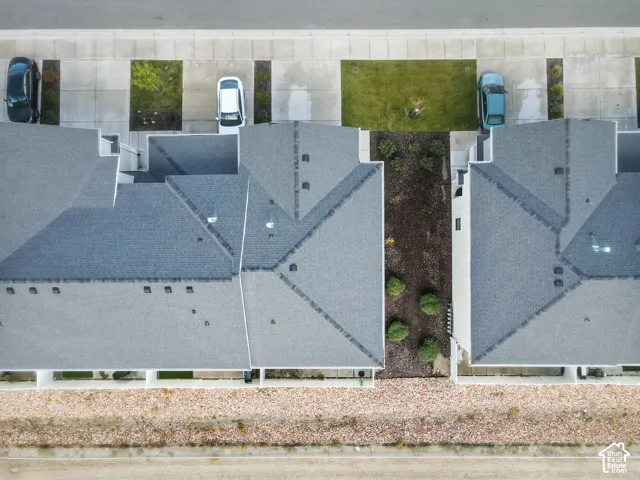 Aerial perspective of the property featuring a multi-pitched shingle roof, concrete driveway, and low-maintenance landscaping with rock ground cover