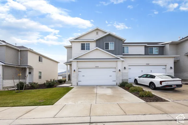 Two-story exterior featuring a mix of horizontal siding and vertical paneling, stone masonry accents, a concrete driveway, and attached multi-car garage