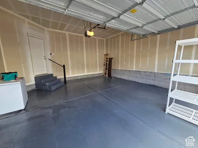 Two-car garage featuring a smooth epoxy-coated concrete floor, an overhead door opener, and a set of interior stairs with a black metal handrail