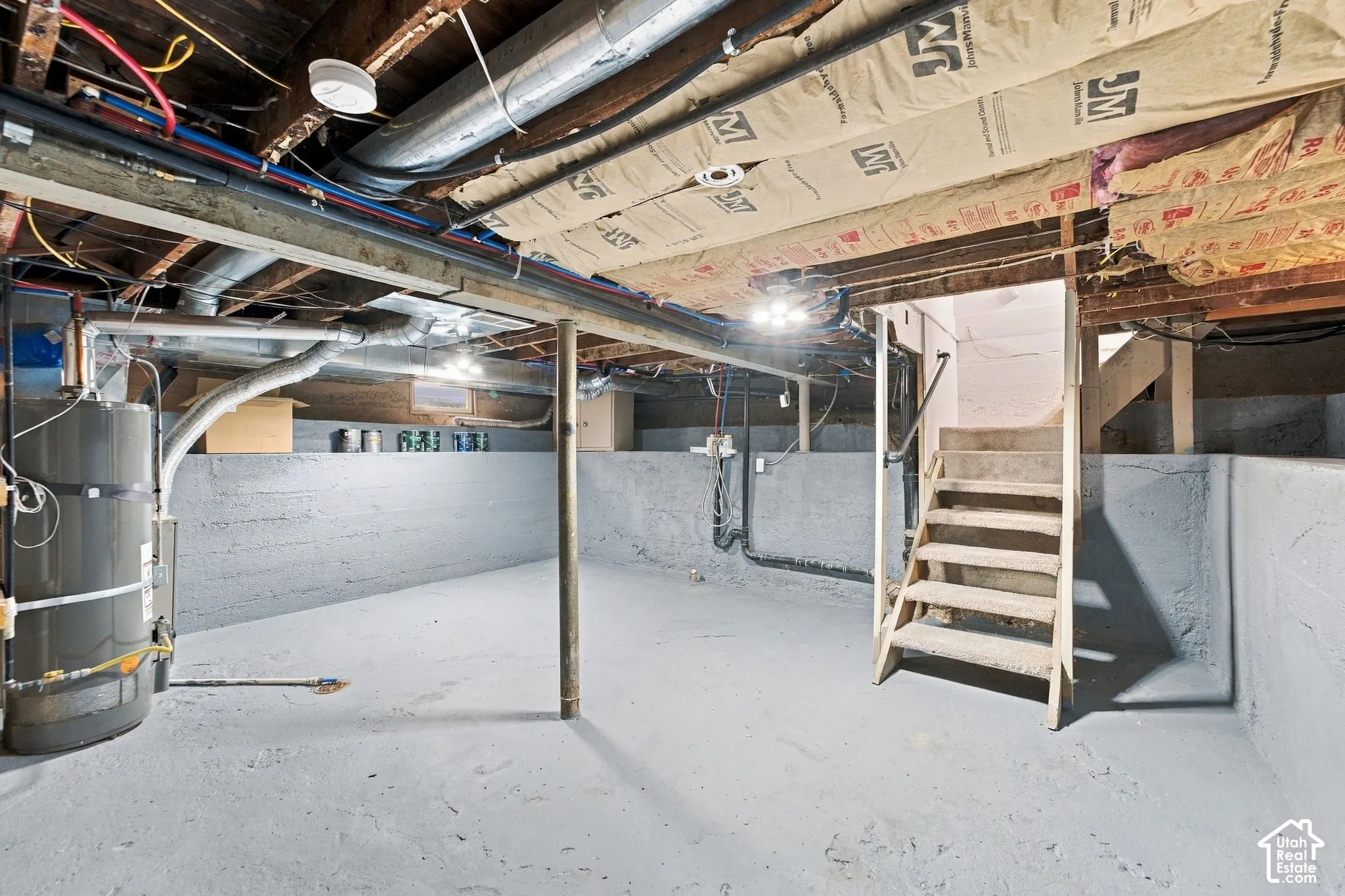 Unfinished basement featuring concrete flooring, painted foundation walls, exposed ceiling joists with insulation, and a water heater
