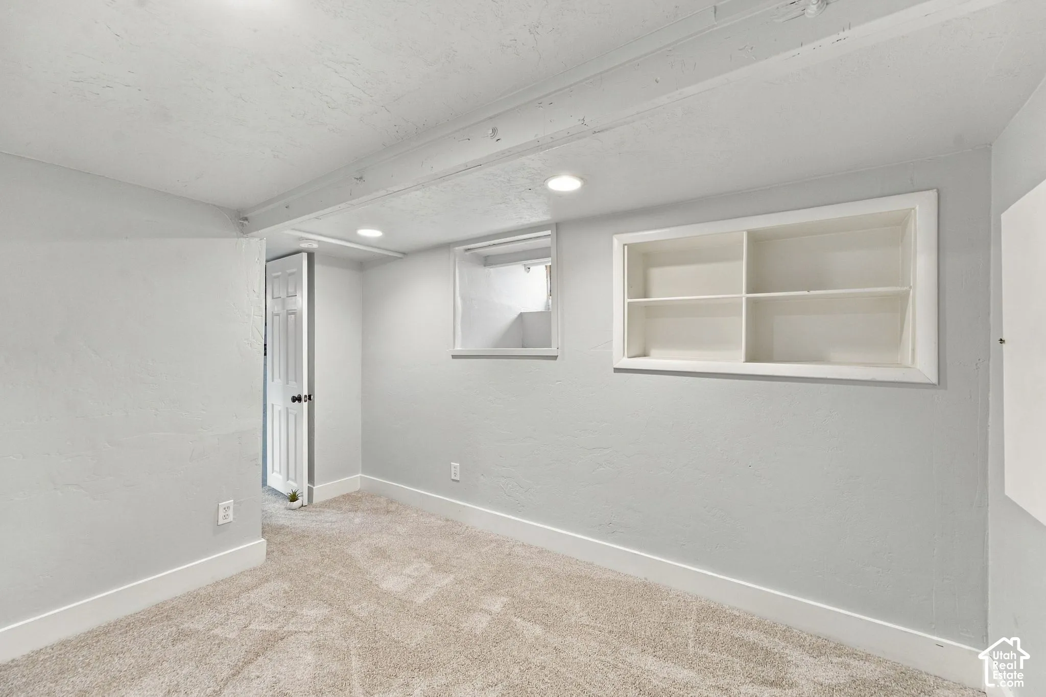 Neutral-toned interior space featuring wall-to-wall carpeting, recessed ceiling lighting, a built-in recessed wall shelf, and a single-pane window