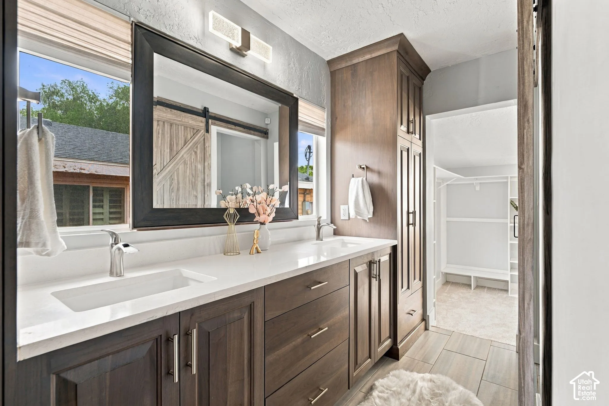 Dual-sink vanity with stone-surface countertop, dark wood cabinetry, tall built-in storage tower, large wall-mounted mirror, and rectangular under-mount sinks