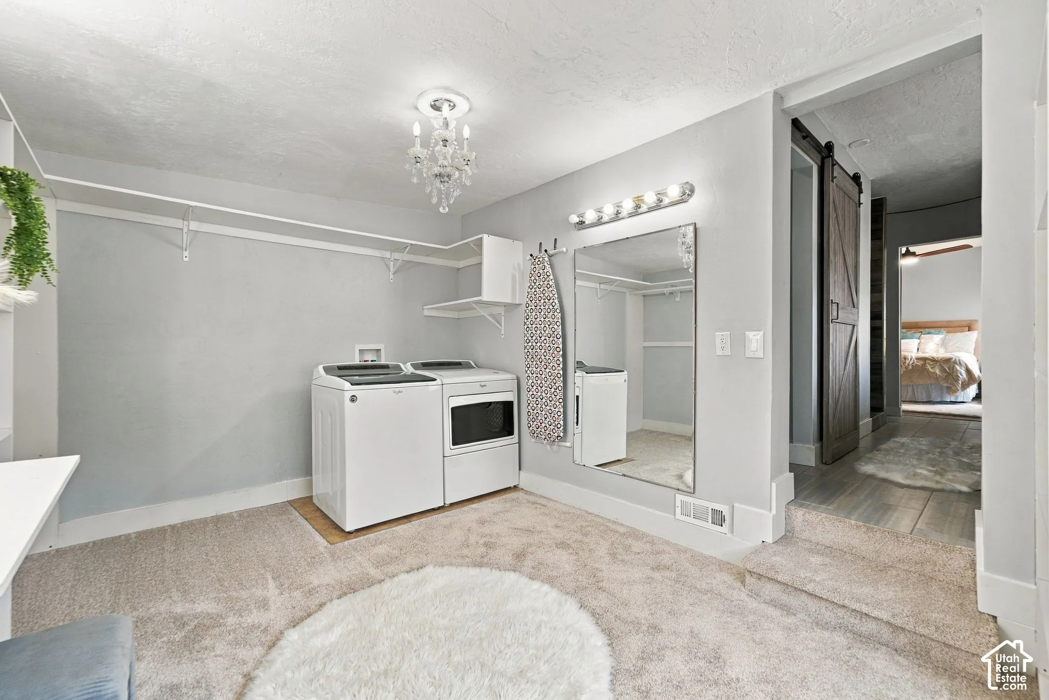 Laundry space featuring integrated wall-mounted shelving, a crystal-style chandelier, a wall-mounted vanity mirror with integrated lighting, and a sliding wood-finish barn door